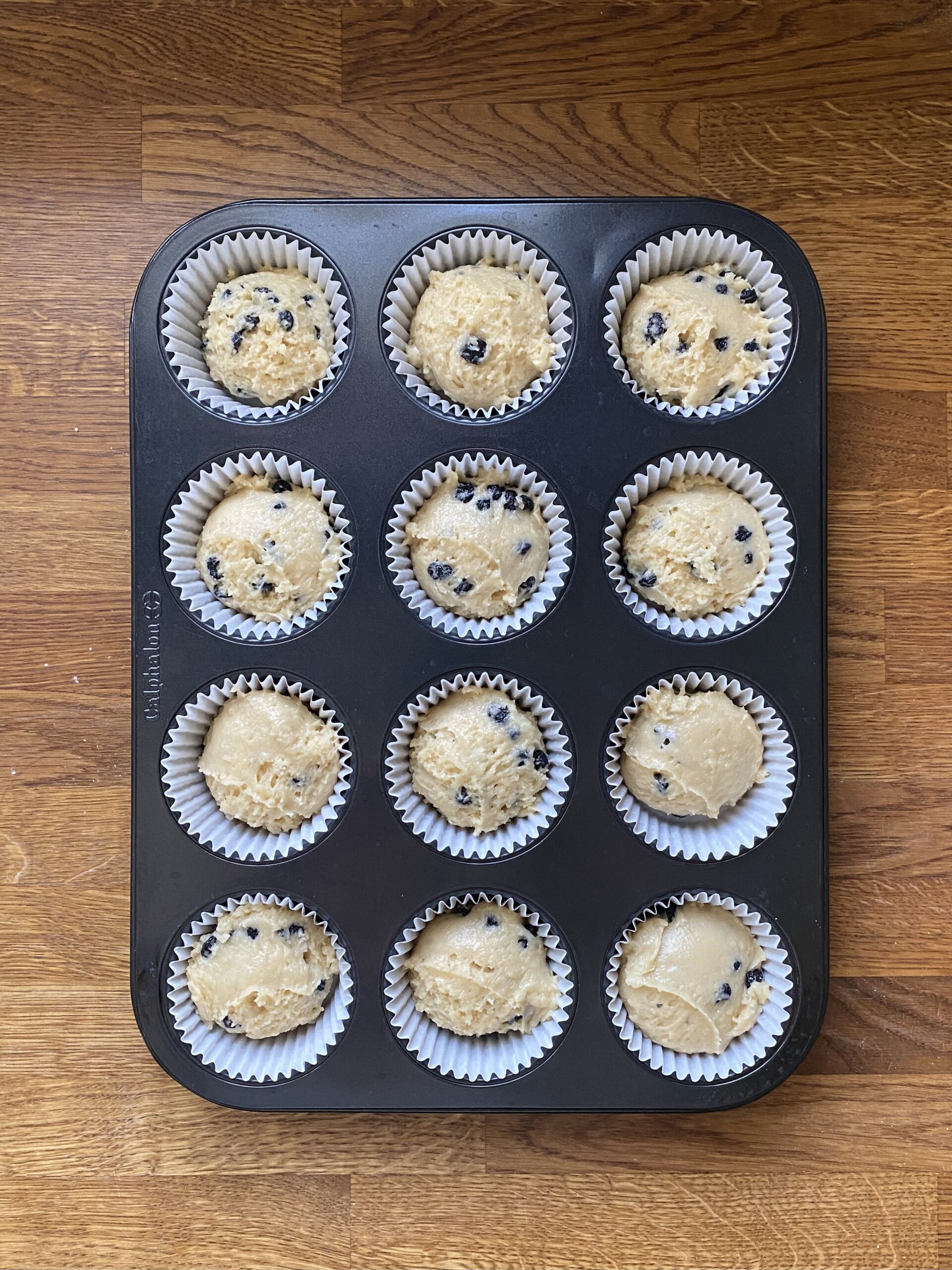 Blueberry muffin batter divided between muffin cups ready to bake.