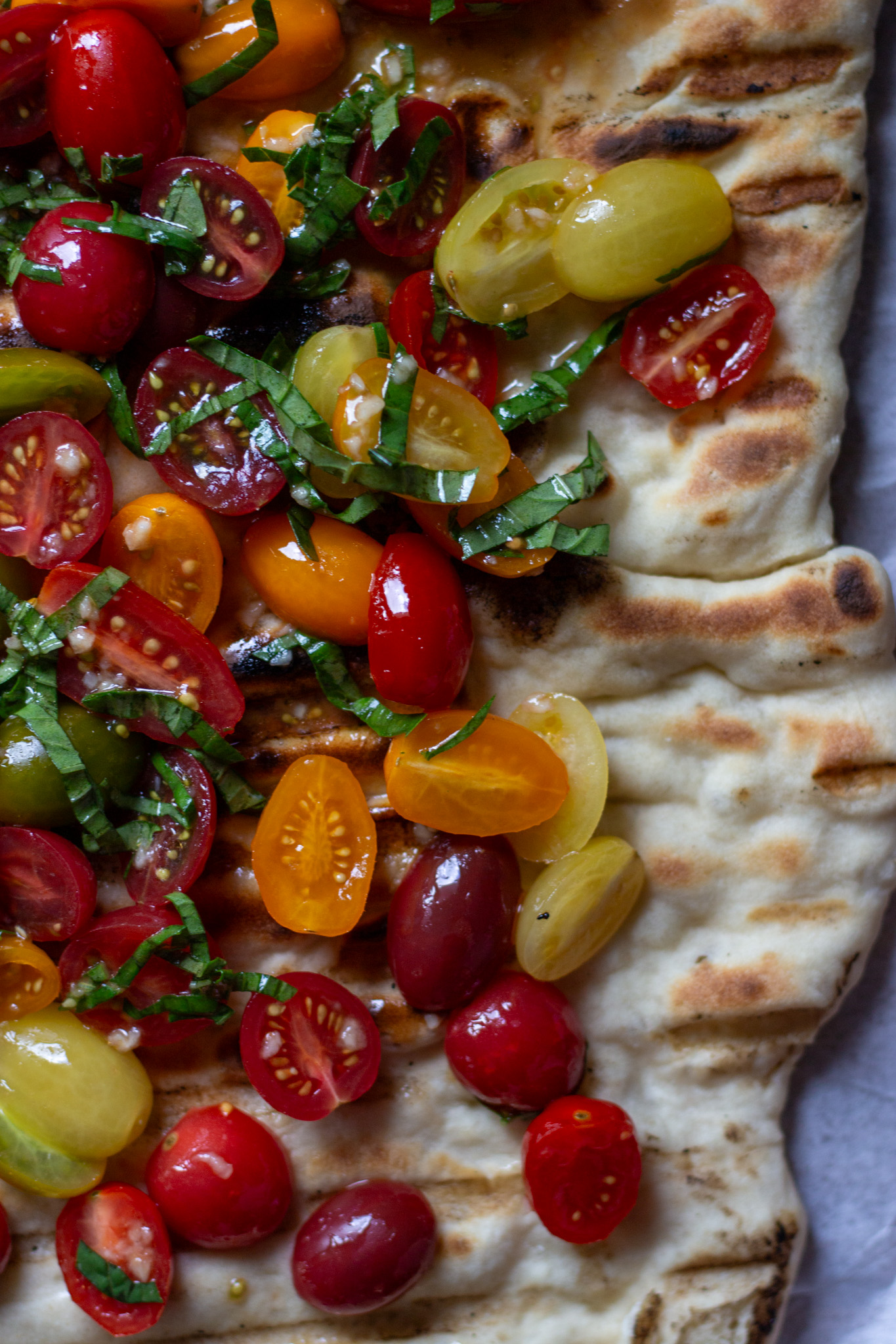 Grilled sourdough discard flatbread topped with bruschetta made with colorful grape tomatoes.