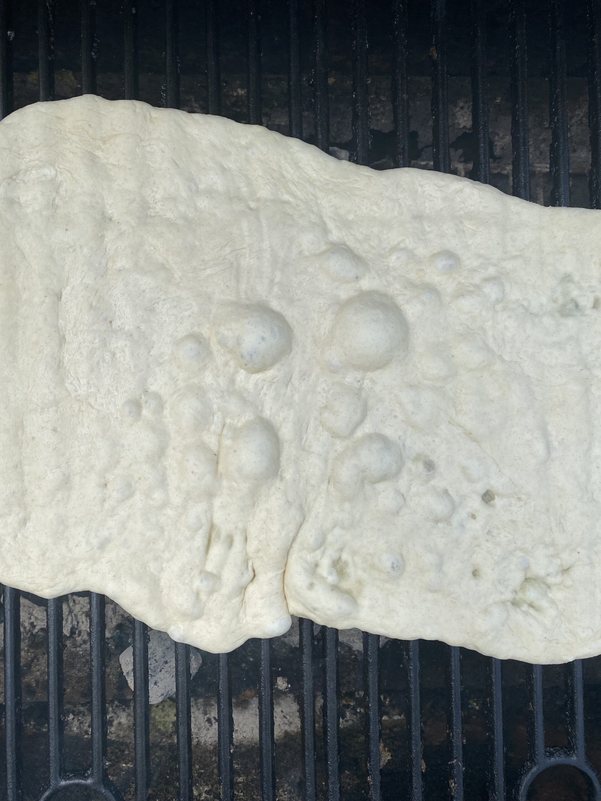 Flatbread on the grill with lots of bubbles forming on the top of the dough.