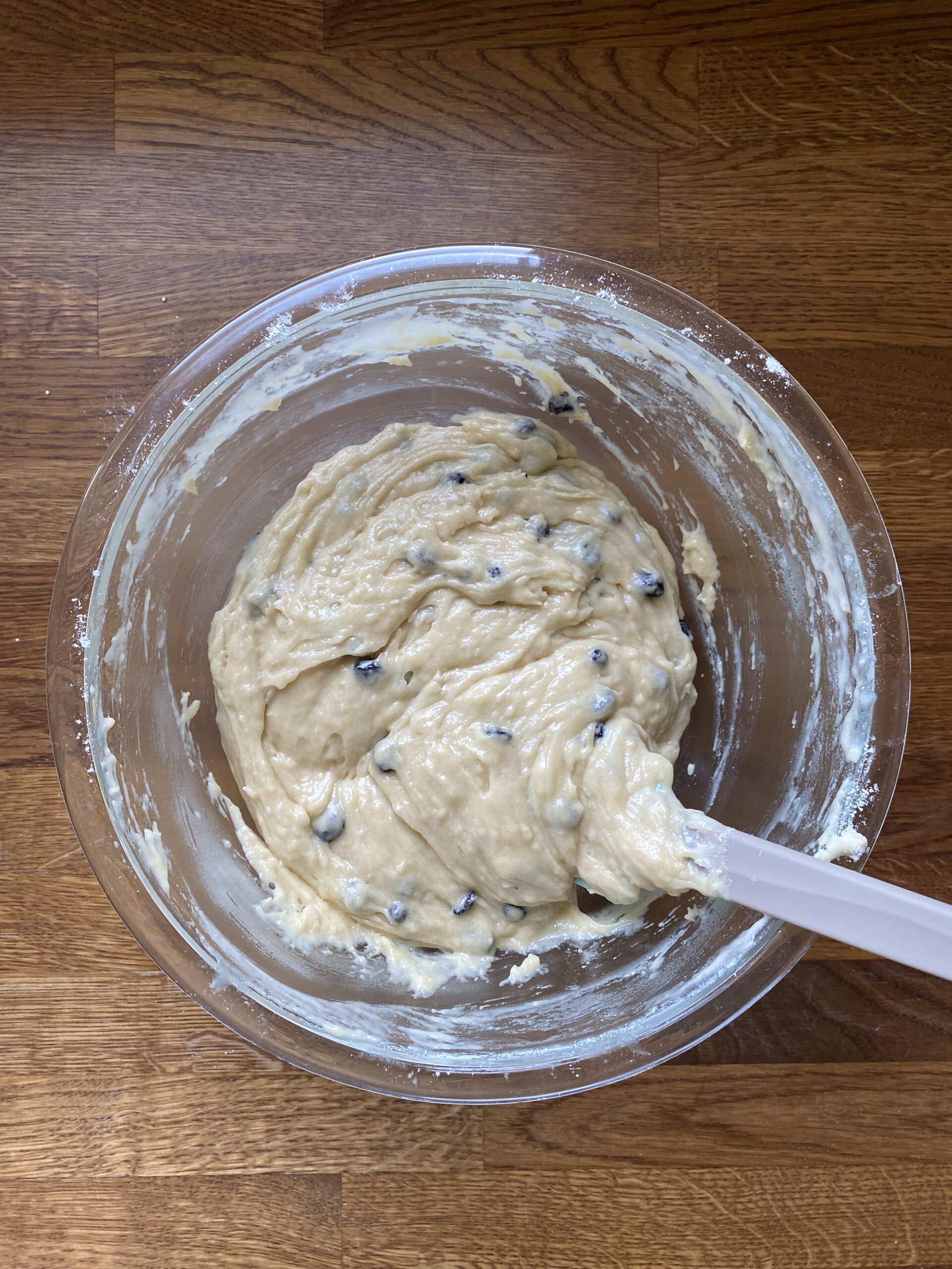 Blueberries mixed into muffin batter in a glass bowl.