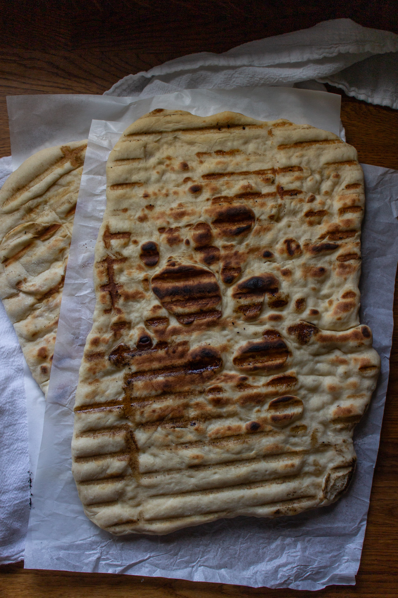 Two large sourdough discard flatbreads fresh off the grill, with grill lines and charred bubbles.