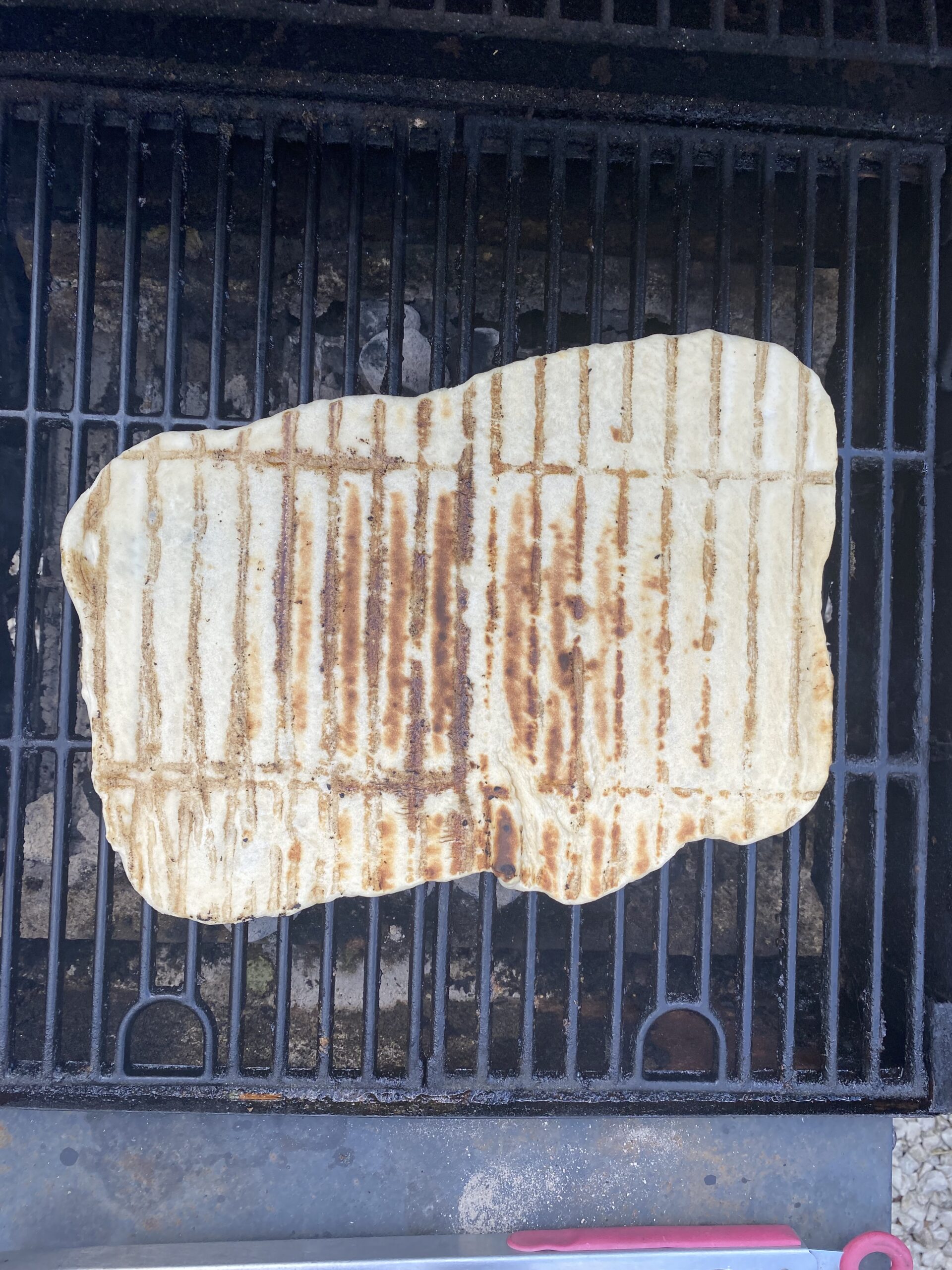 Flatbread on the grill after flipping, with grill grate lines on the top.