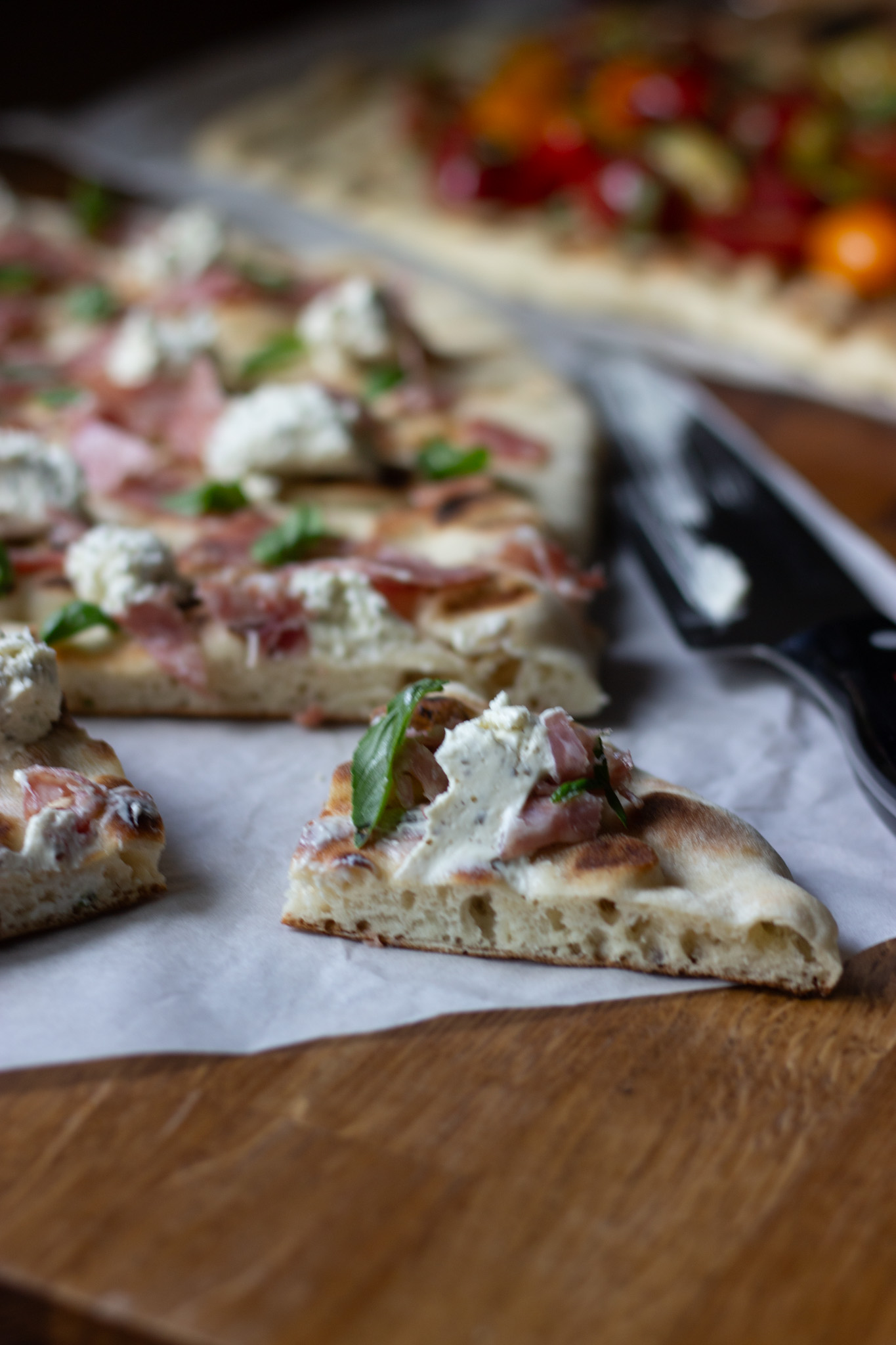 Slice of sourdough discard flatbread topped with herby cheese, salami, and fresh basil, ready to eat.