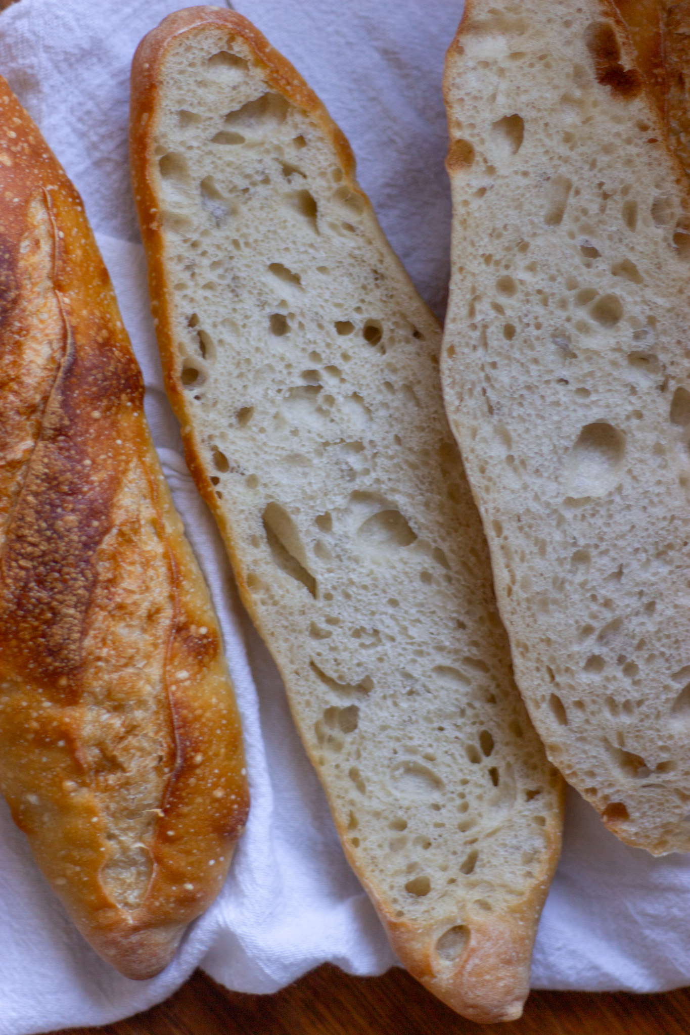Freshly baked baguette next to a baguette sliced down the middle to show the open crumb.